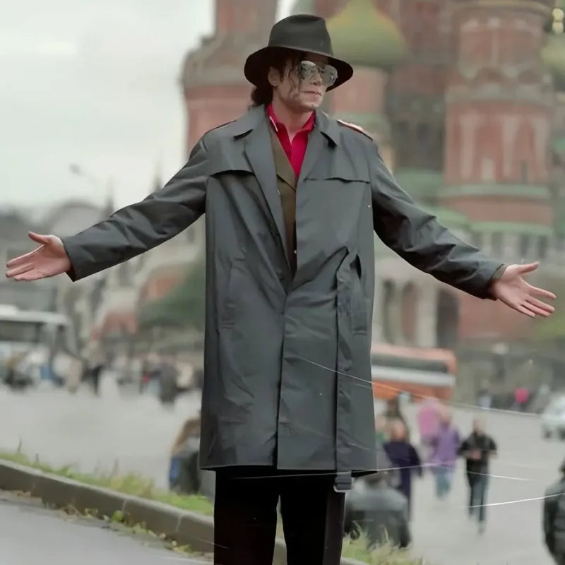 Person in a gray trench coat and hat standing on a city street with blurred background