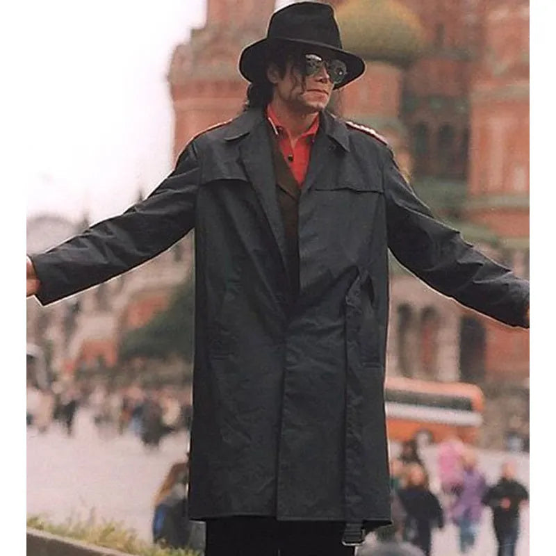 Person wearing a black coat and hat with arms outstretched, blurred background